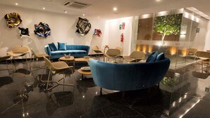 Een moderne lobby met een blauwe bank, beige stoelen en abstracte muurkunst.