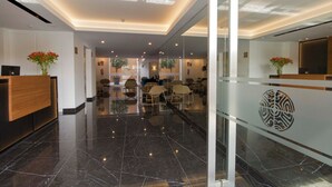 Een moderne hotellobby met een receptiebalie, een zithoek en een glazen scheidingswand.