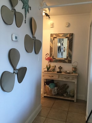 Un couloir doté d’un ventilateur de plafond, d’un miroir fixé au mur et d’une petite console sur laquelle sont disposés des objets décoratifs.