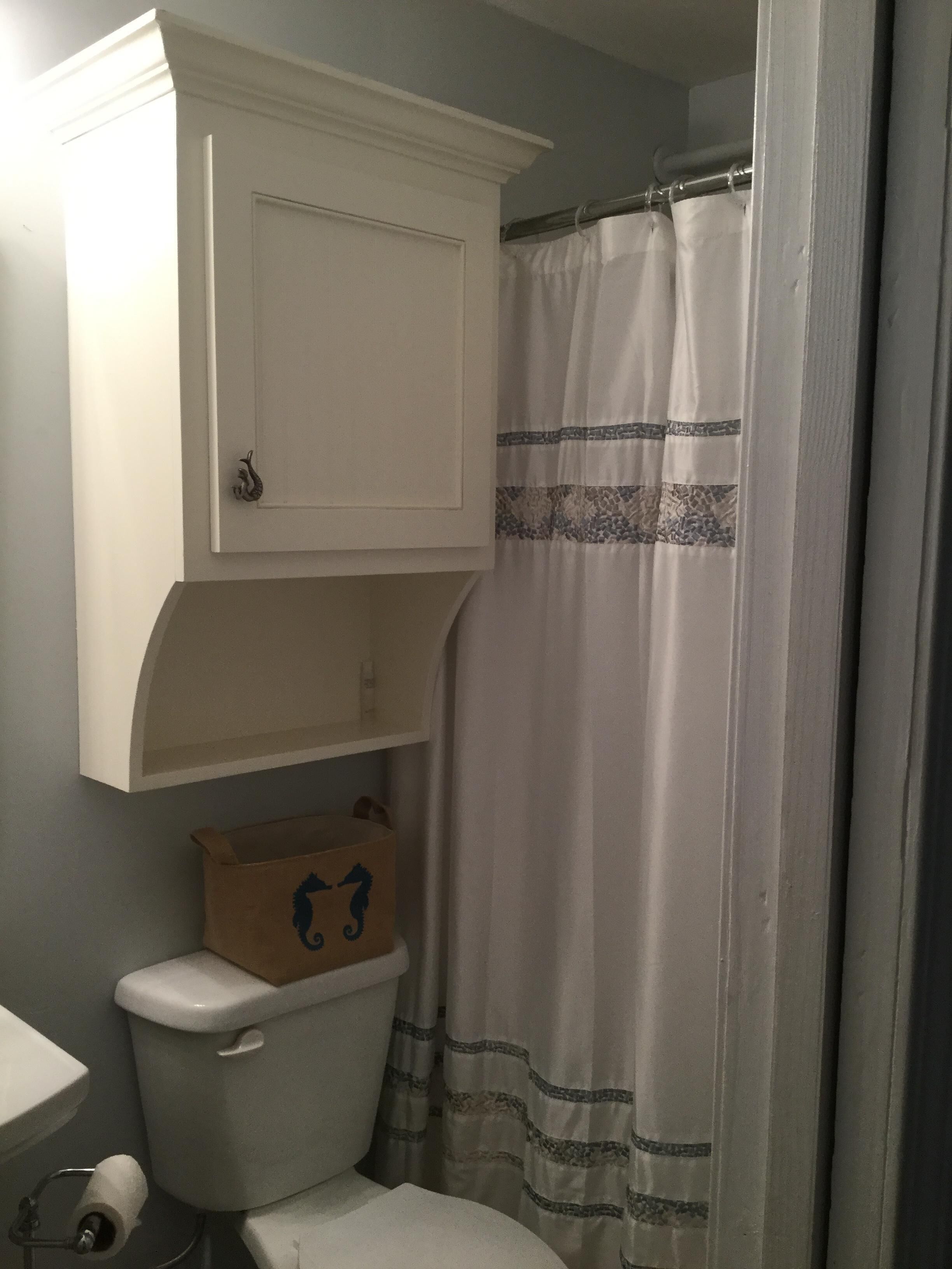 A bathroom with a toilet, a cabinet above the toilet, and a shower curtain.