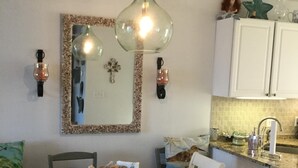 Un comedor con una mesa redonda, sillas y una araña. Hay una zona de cocina con armarios y un fregadero.