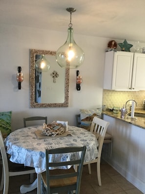 Un coin repas comprenant une table ronde, des chaises et un lustre. Il y a également un espace cuisine avec des placards et un évier.