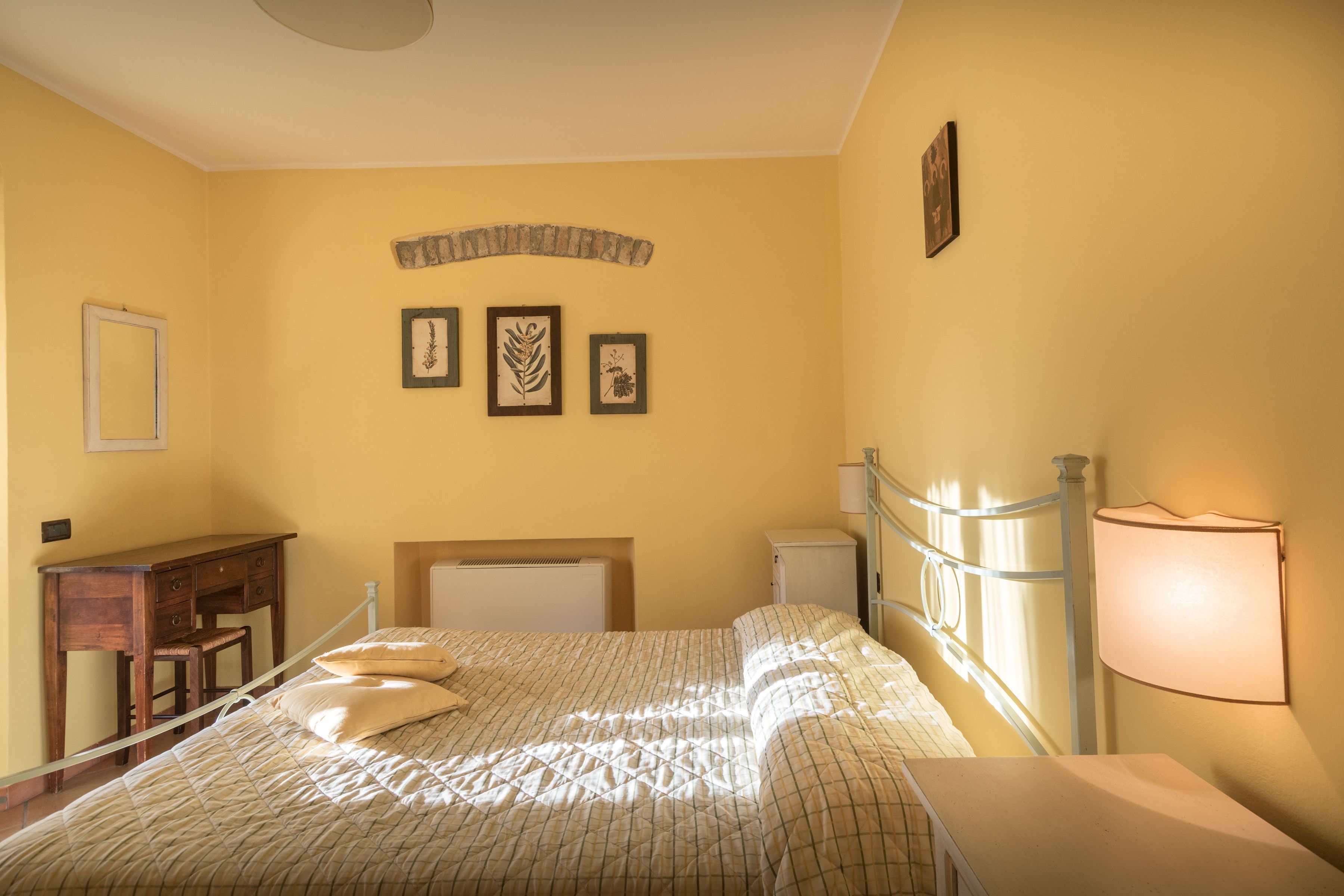 A bedroom with a bed, bedside table, lamp, dresser, and wall-mounted pictures.