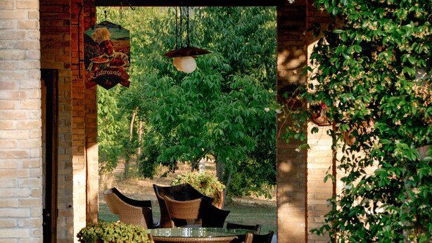 An outdoor patio with wicker furniture, a hanging light fixture, and a brick wall. - Agriturismo Il Giardino dei Ciliegi (Assisi)