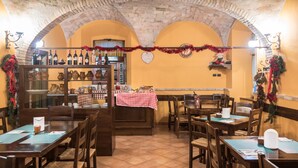 A restaurant with brick arches, wooden tables, and chairs. There are wine bottles on shelves and a Christmas decoration. - Agriturismo Il Giardino dei Ciliegi (Assisi)