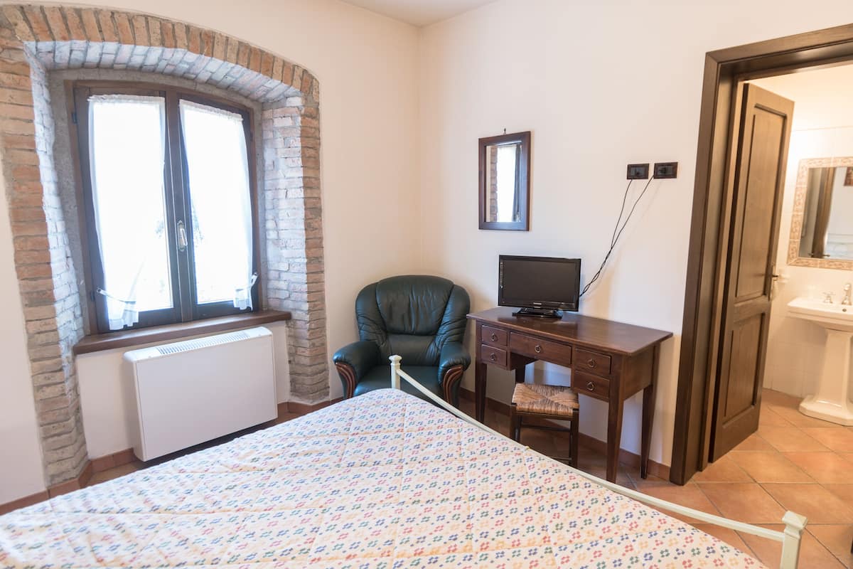 Une chambre à coucher comprenant un lit, un bureau, une chaise, un téléviseur et une salle de bain avec un lavabo.