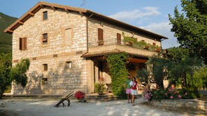 A stone building with a balcony, surrounded by greenery and flowers. - Agriturismo Il Giardino dei Ciliegi (Assisi)