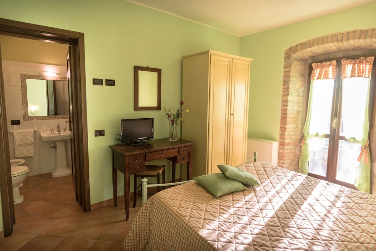 Une chambre à coucher comprenant un lit, un bureau, une chaise, une armoire et une salle de bain visible à travers une porte ouverte.