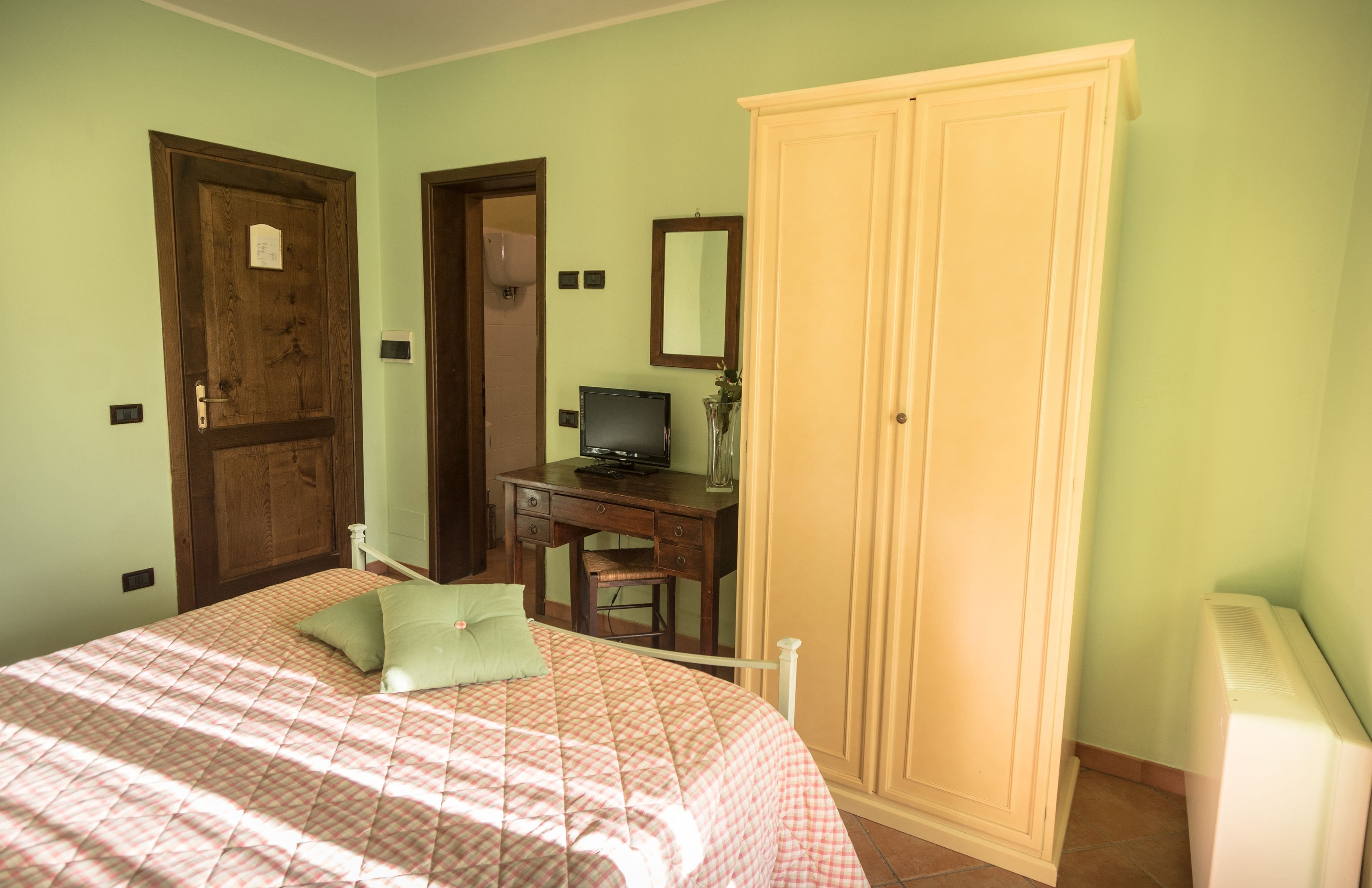 Een slaapkamer met een bed, een bureau, een televisie en een kledingkast.