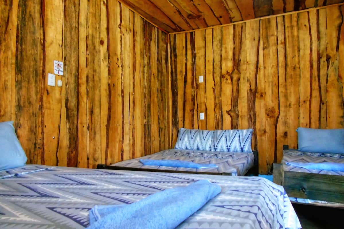A room with wooden walls, two beds with patterned bedding, and a small wooden table.