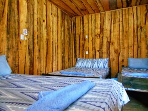 Una habitación con paredes de madera, dos camas con ropa de cama estampada y una pequeña mesa de madera.
