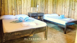 A rustic room with two wooden beds, each with a white mattress and pillows, and a small wooden nightstand between them. - El Tesoro de Sir Hotel (Drake Bay)