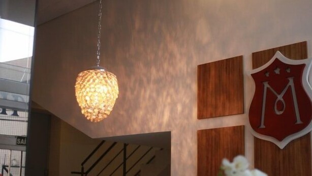 Un interior moderno con una lámpara colgante texturizada, un panel de pared de madera y un logotipo con forma de escudo con la letra 'M'.