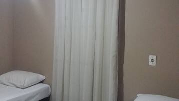 Quarto com duas camas, uma cortina, um interruptor de luz e chão revestido de azulejos.