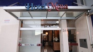 La entrada del Hotel Maia, con fachada de vidrio y una recepción visible en el interior.