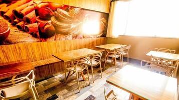 Um restaurante com mesas e cadeiras de madeira, um grande mural na parede e uma janela com cortinas.