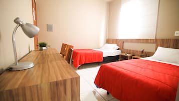 Habitación de hotel con dos camas, un escritorio con lámpara, una mesita con una planta y una mesita de noche.