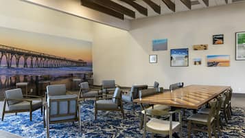 A conference room with a large wooden table and multiple chairs, a blue patterned carpet, and a mural of a pier on the wall.