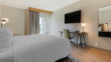 Una habitación de hotel con una cama grande, un escritorio con una silla, un televisor de pantalla plana montado en la pared y un espejo amplio.