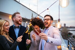 A group of people holding sparklers on a rooftop with string lights and a city view in the background. - Four Points by Sheraton Myrtle Beach (Myrtle Beach)