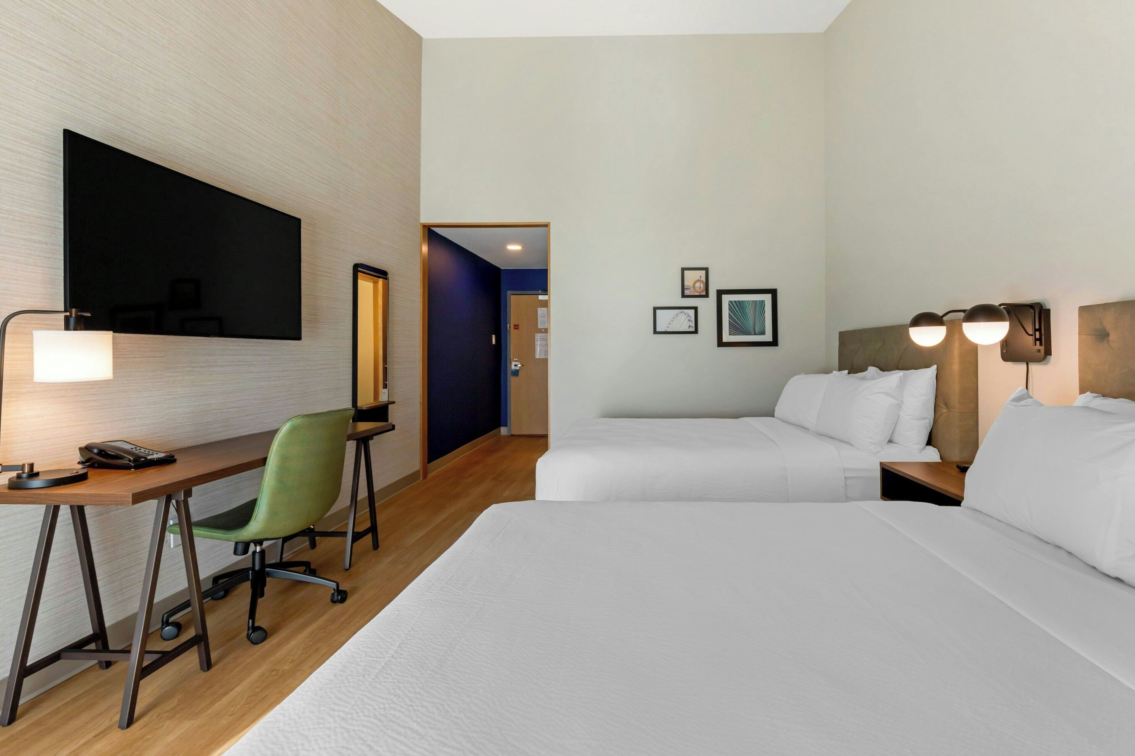 Une chambre d’hôtel équipée d’un bureau, de deux lits, d’une chaise et d’un téléviseur.