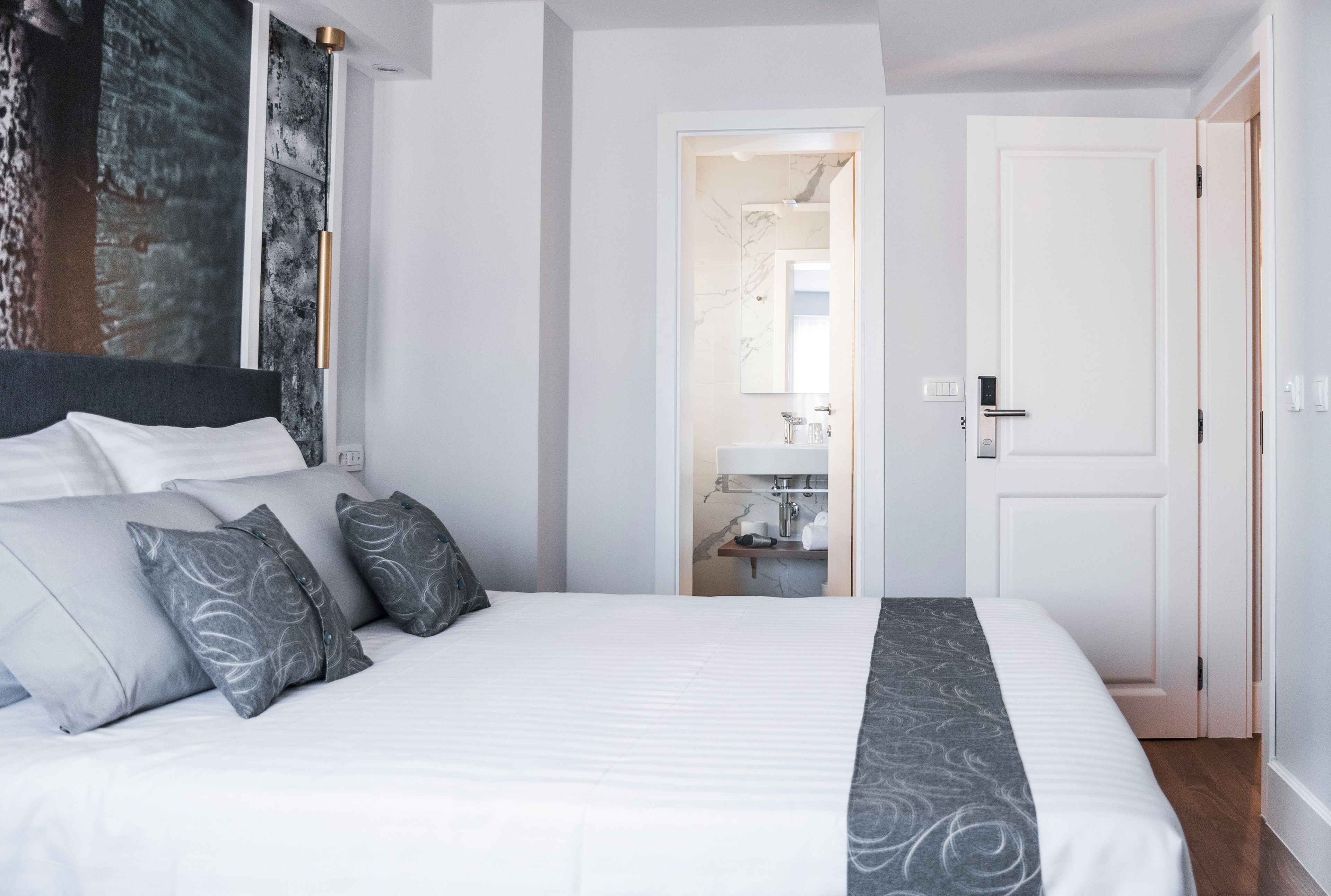 A modern hotel room with a large bed, a bathroom visible through an open door, and a minimalist design.