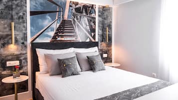 Une chambre d’hôtel moderne avec un grand lit, une vue sur un pont et une petite table sur laquelle se trouvent un livre et une fleur.