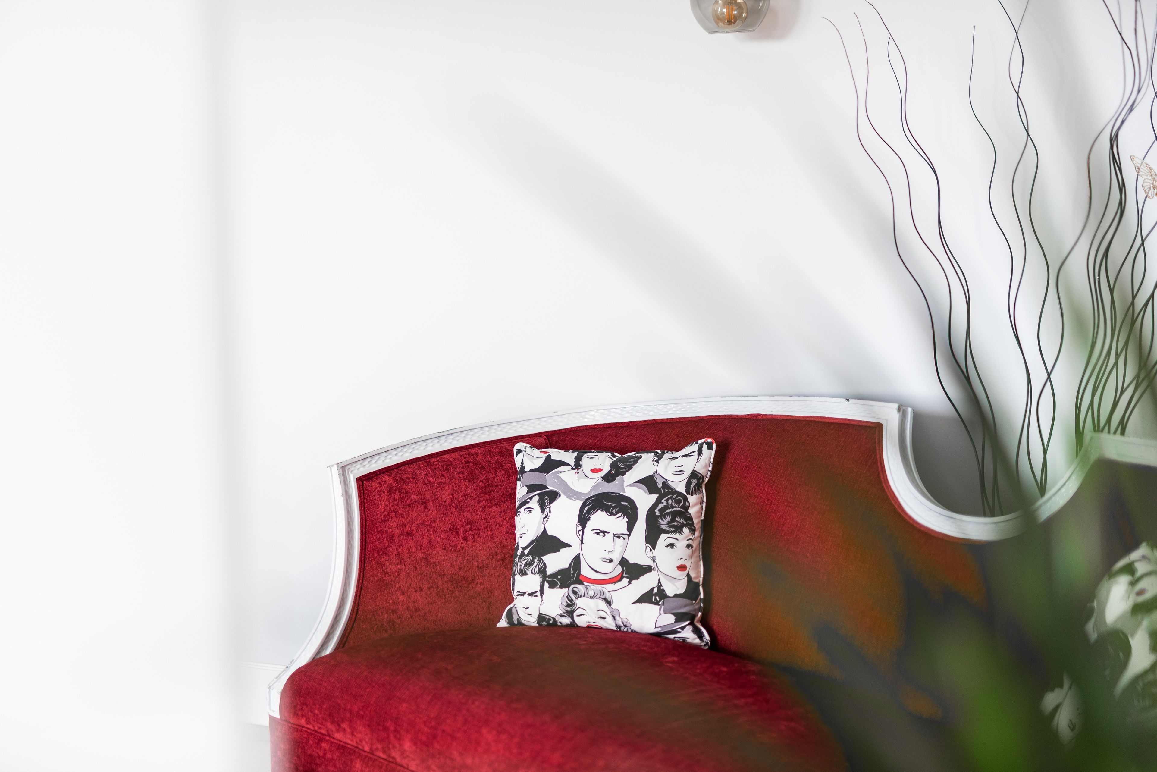 Un sofá de terciopelo rojo con un cojín estampado frente a una pared blanca.