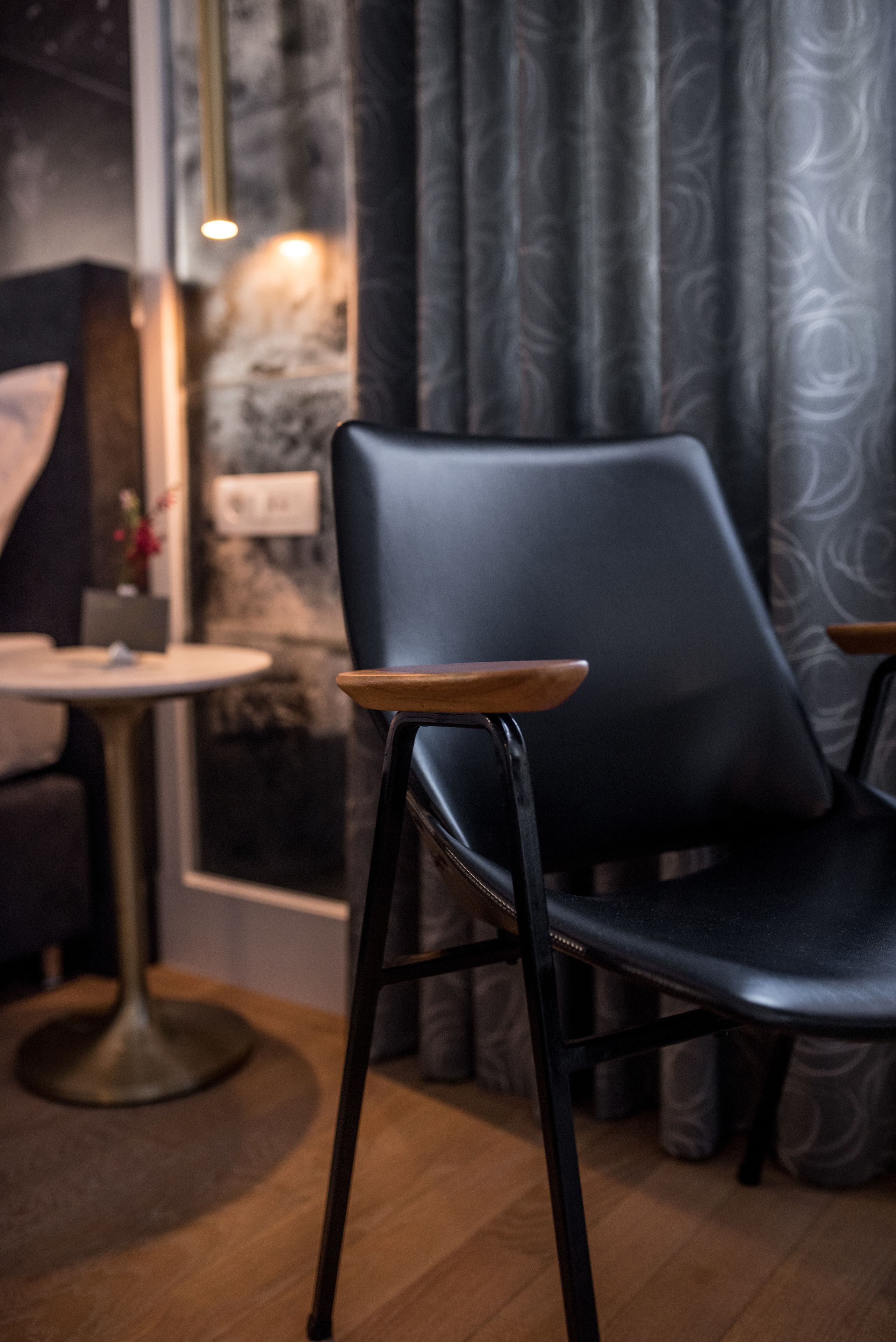 A modern interior with a black leather chair, a round table, and patterned curtains.