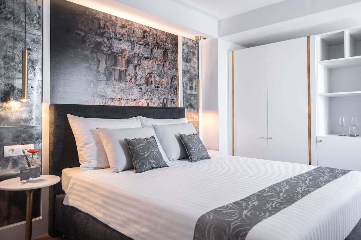 A modern hotel room with a large bed, a stone accent wall, and a white wardrobe with shelves.