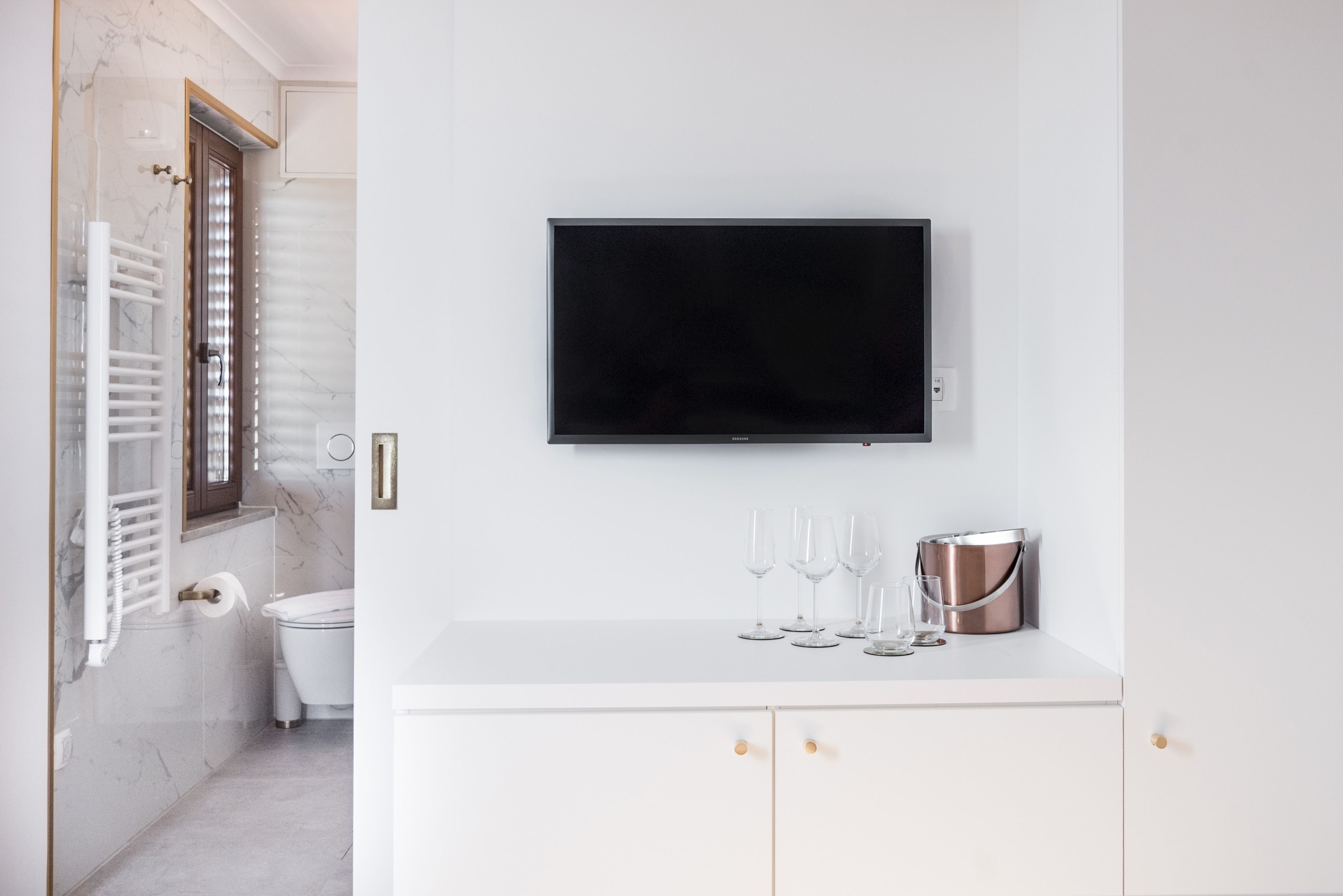 A modern bathroom with a white vanity, a mounted TV, and a shower area with a glass door.