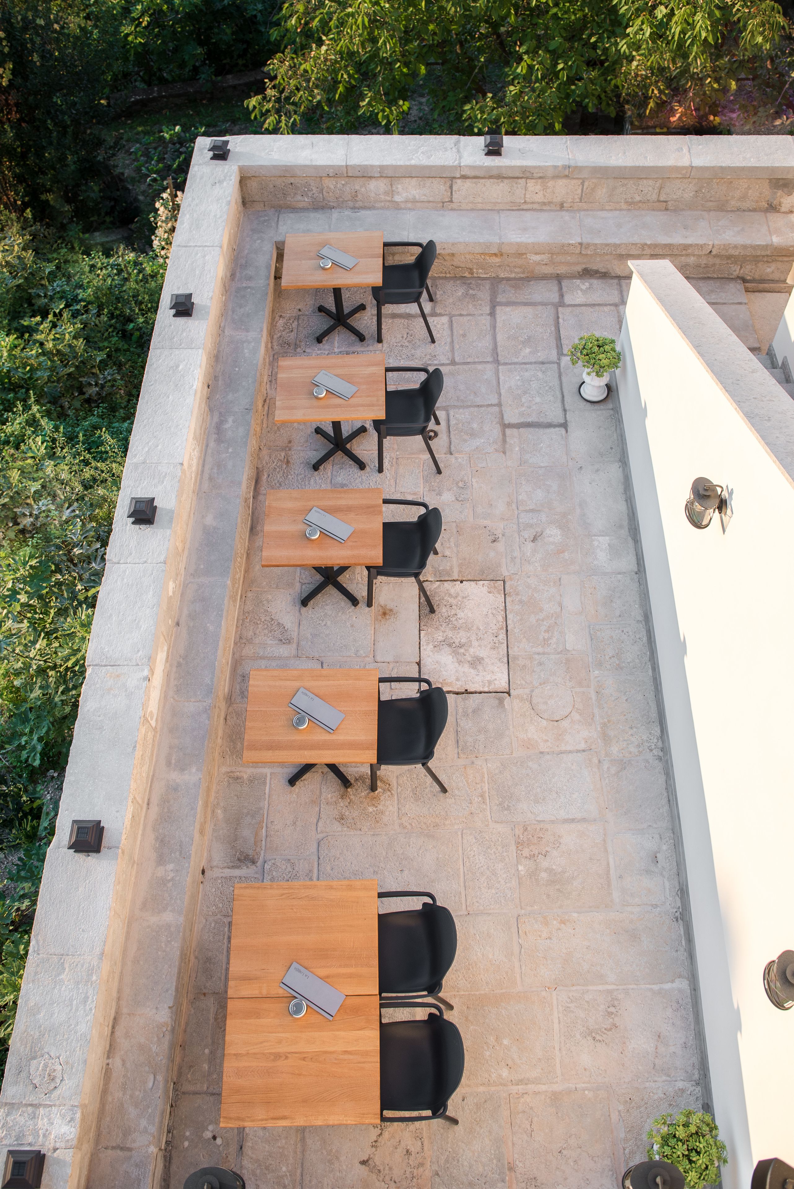 Un patio al aire libre con seis mesas de madera y sillas negras, dispuestas en dos filas.