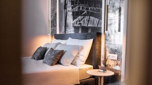 A neatly made bed with a white comforter and several patterned pillows, a small bedside table with a lamp, and a wall-mounted power outlet. - La Loggia Diffused Hotel (Labin)