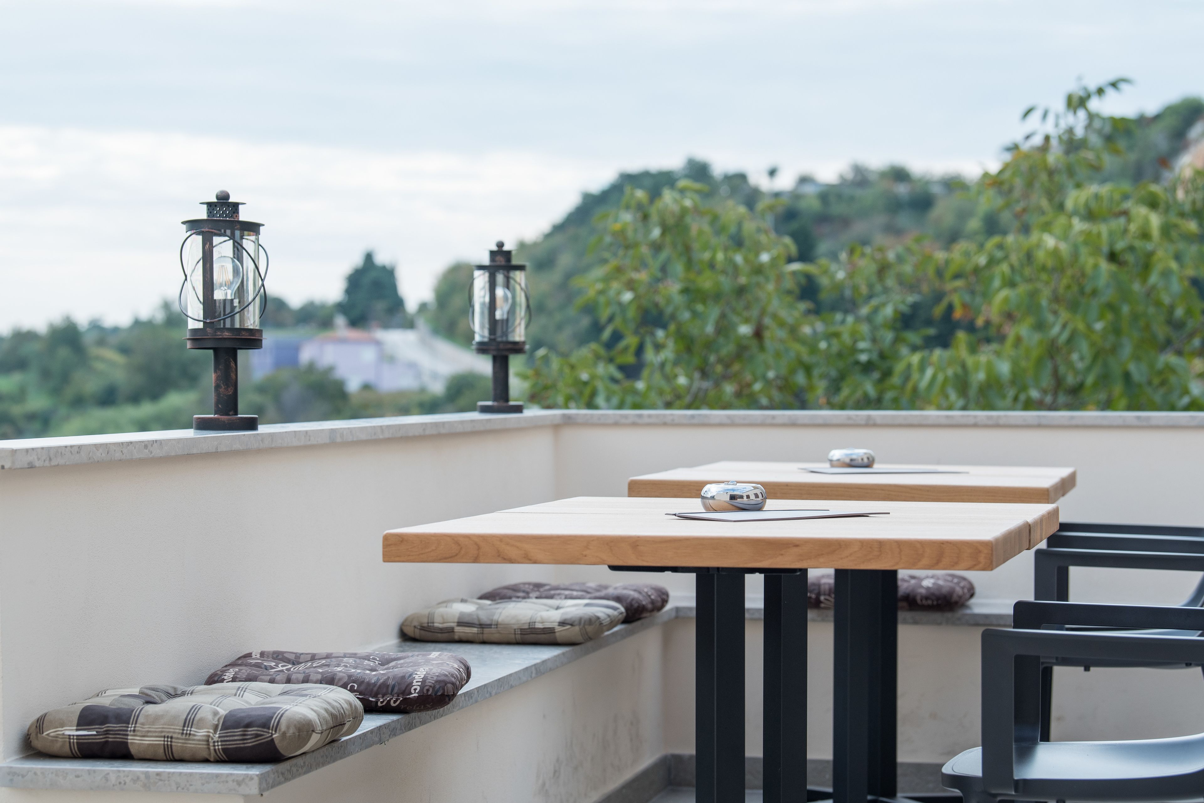 Een dakterras met twee houten tafels, zwarte metalen stoelen en decoratieve lantaarns.