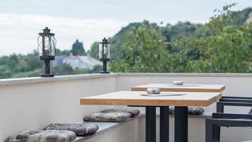 A rooftop terrace with two wooden tables, black metal chairs, and decorative lanterns.