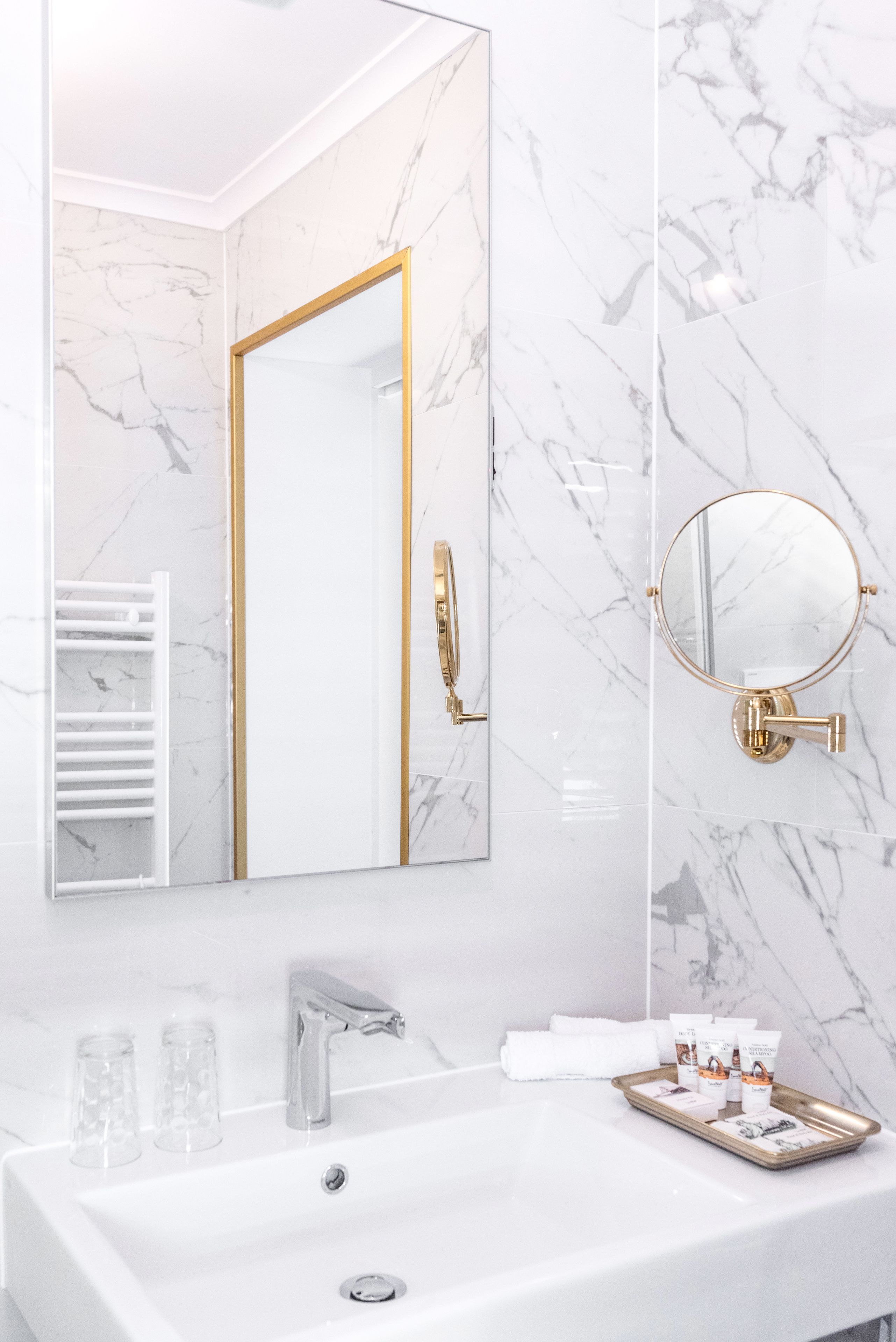 Un baño con lavamanos de mármol blanco, un espejo grande y un grifo dorado.