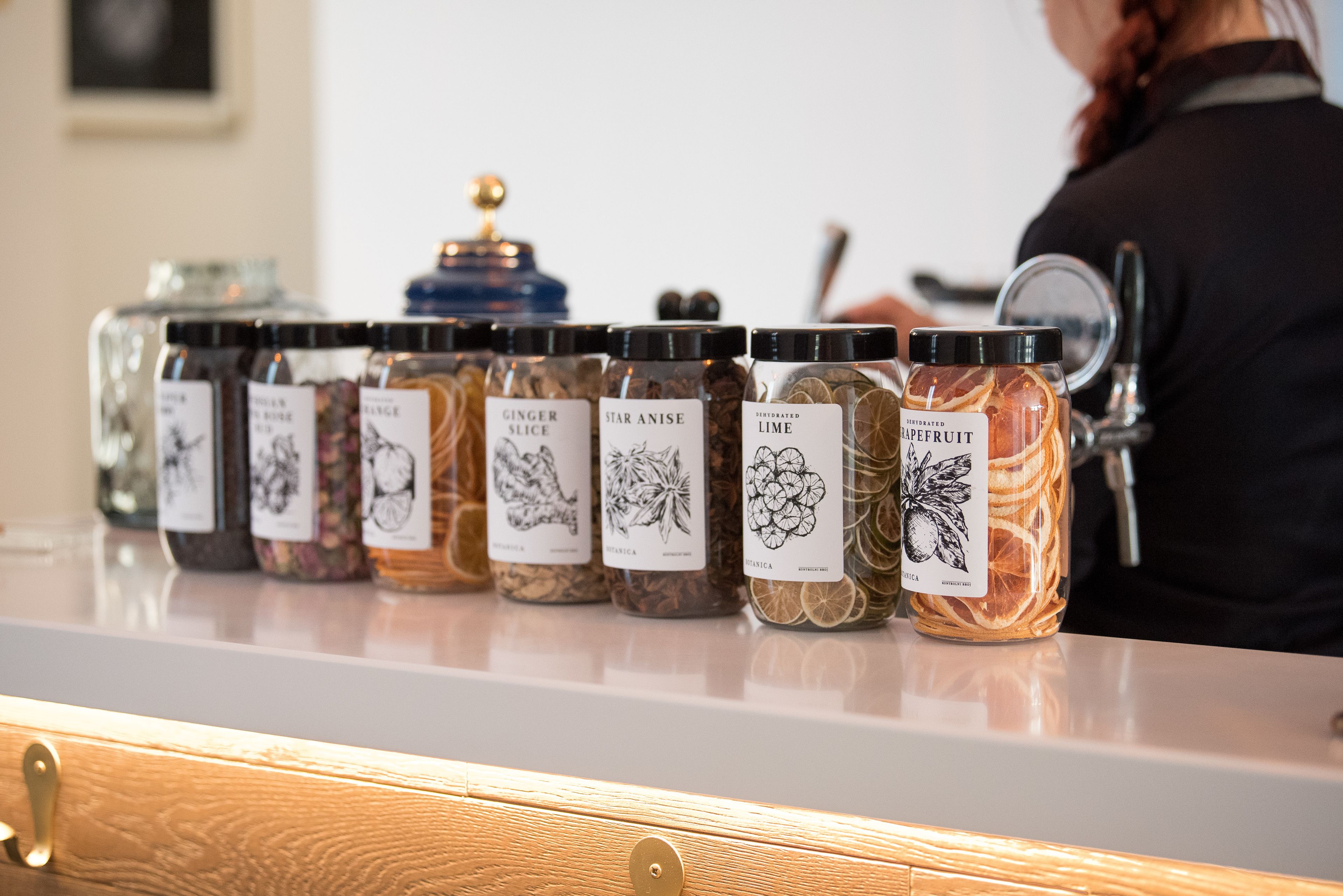Une rangée de bocaux en verre, chacun portant une étiquette, est posée sur un comptoir et contient différentes épices.
