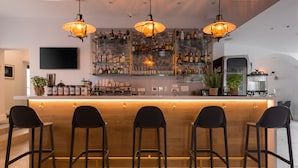 A bar area with a wooden counter, three black bar stools, and hanging pendant lights. - La Loggia Diffused Hotel (Labin)