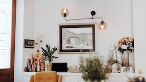 A dining area with a white table, a yellow chair, and a pendant light. There is a framed picture on the wall and a vase with flowers on the table. - La Loggia Diffused Hotel (Labin)