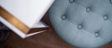 A round, tufted ottoman with a buttoned design, placed on a wooden floor.
