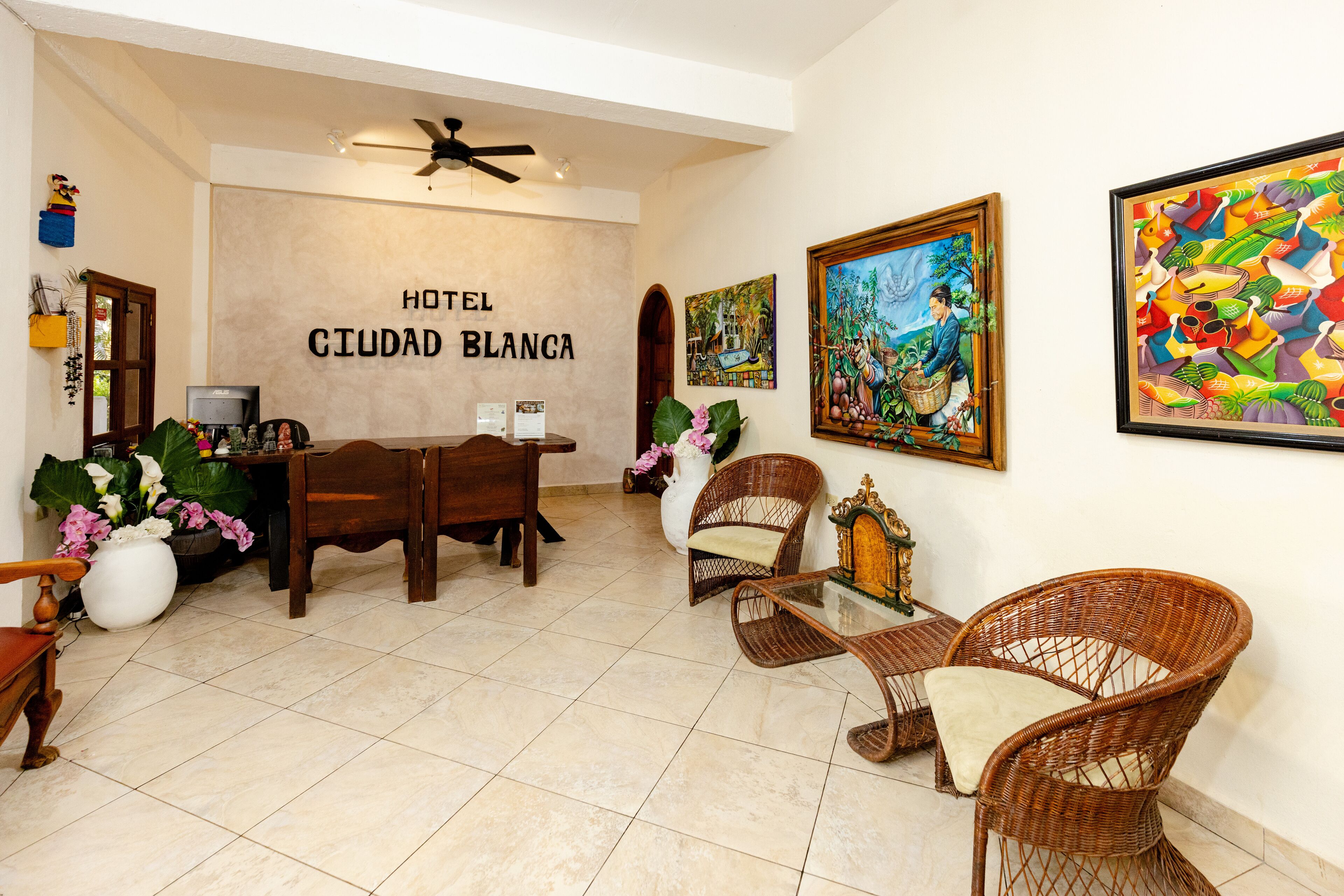 A hotel lobby with a dining area, wicker chairs, a ceiling fan, and artwork on the walls.