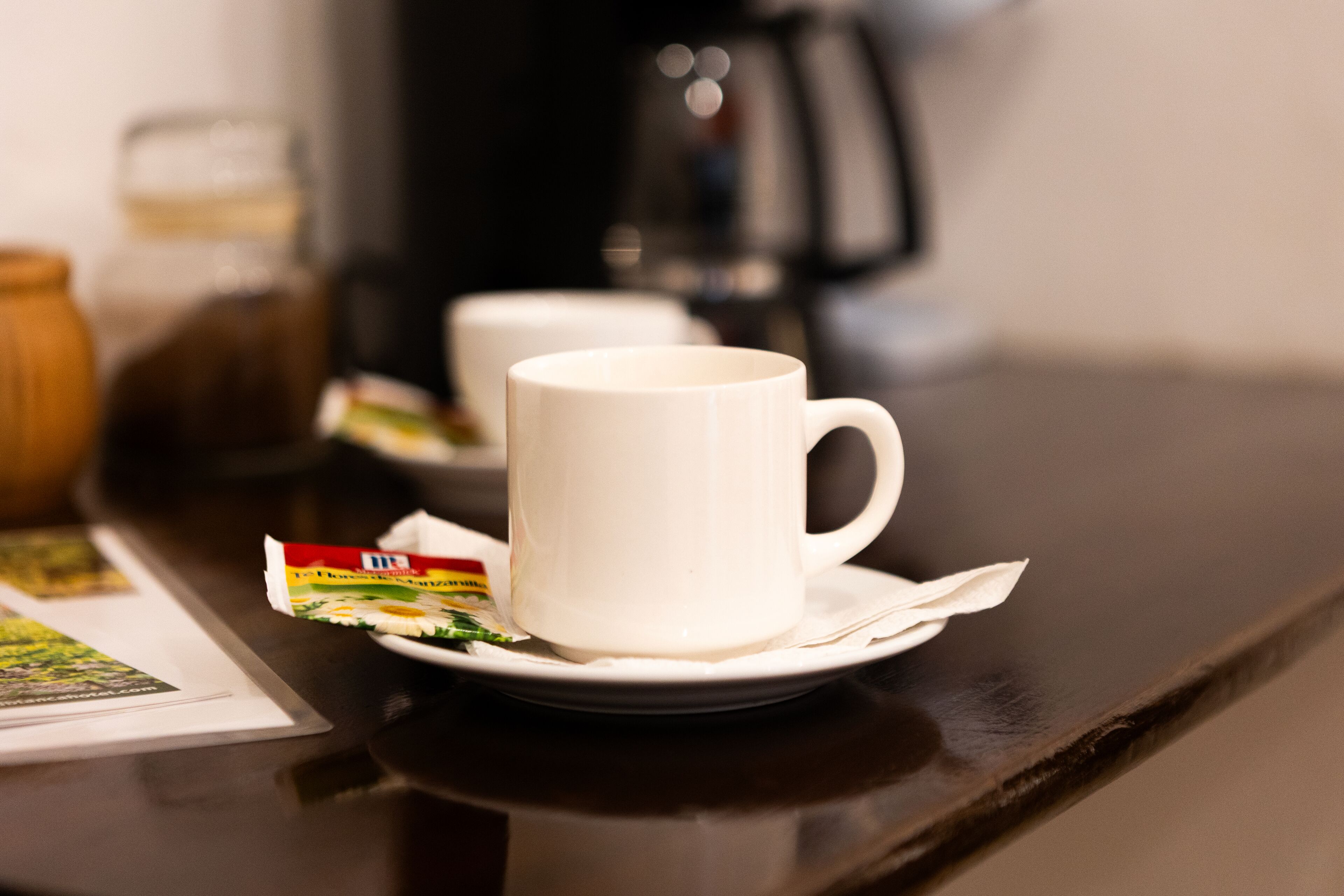 Una tassa de cafè blanca sobre un plat, amb un sobre de mill d'arròs damunt d'una taula.