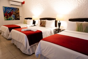 Habitación de hotel con tres camas individuales, cada una con cubrecama rojo y blanco, almohadas blancas y una mesita con lámpara.
