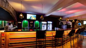 A bar area with a long counter, multiple bar stools, and a television screen mounted on the wall. - Hotel Ciudad Blanca (Copan Ruinas)