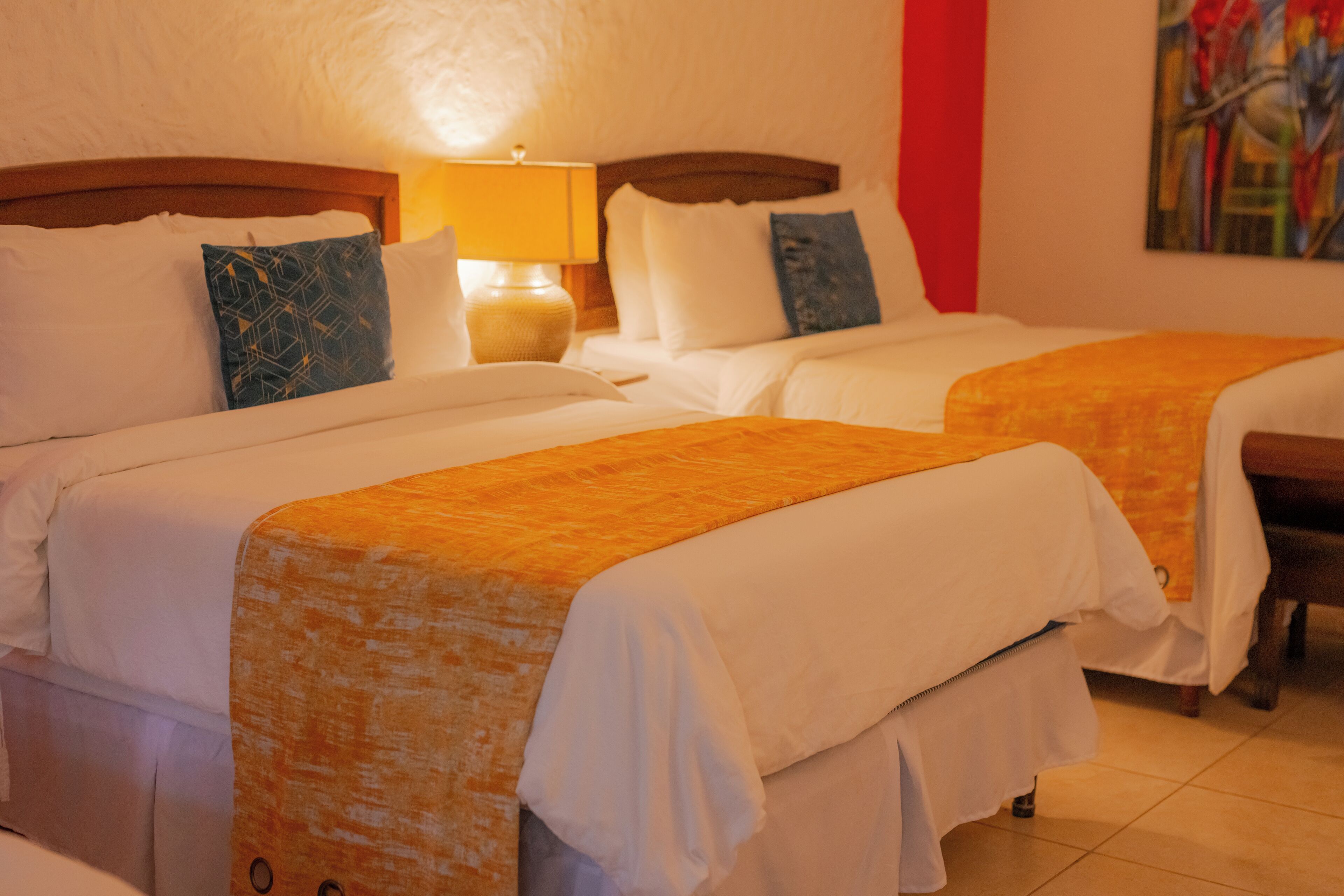 Una habitación de hotel con dos camas, una mesita de noche con una lámpara y un cuadro en la pared.