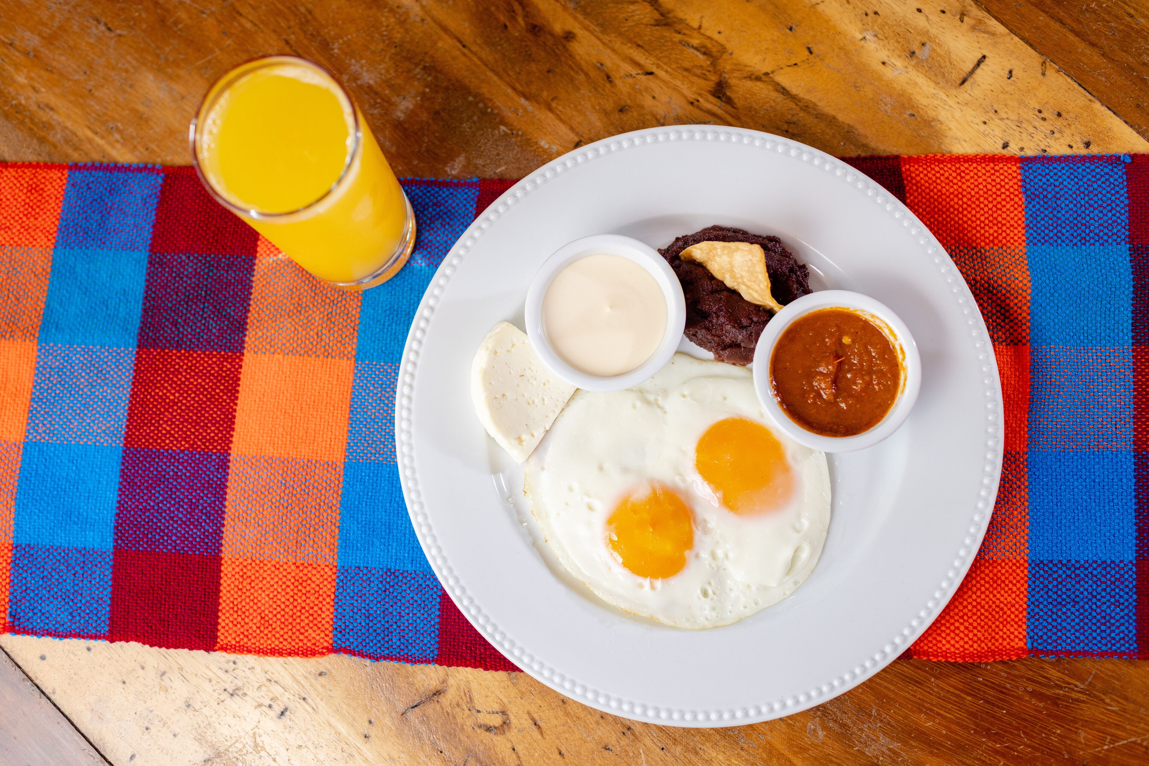 Un plato con huevos, un trozo de carne y dos salsas sobre un mantel a cuadros.