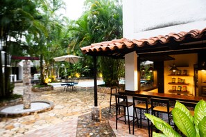 Un patio al aire libre con suelo de piedra, una mesa de madera con sillas y un techo de baldosas.