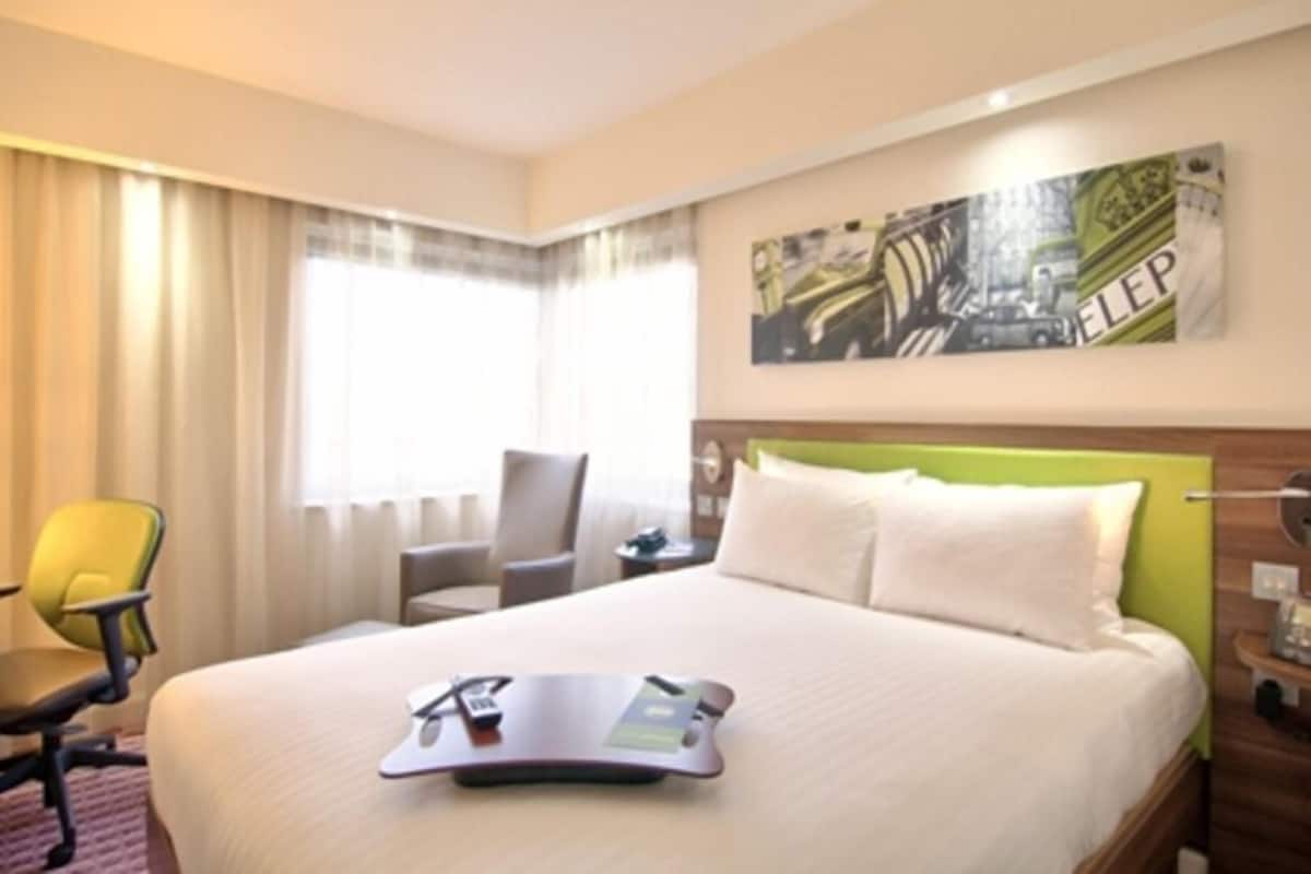 A hotel room with a bed, a desk, a chair, and a window with curtains.