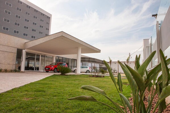 Un edificio moderno con entrada cubierta, zona de estacionamiento y césped cuidado.