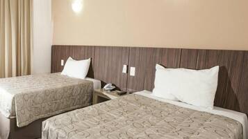Une chambre d’hôtel avec deux lits, chacun agrémenté de draps à motifs, d’une tête de lit en bois, de tables de chevet avec des lampes et d’un rideau sur le côté gauche.